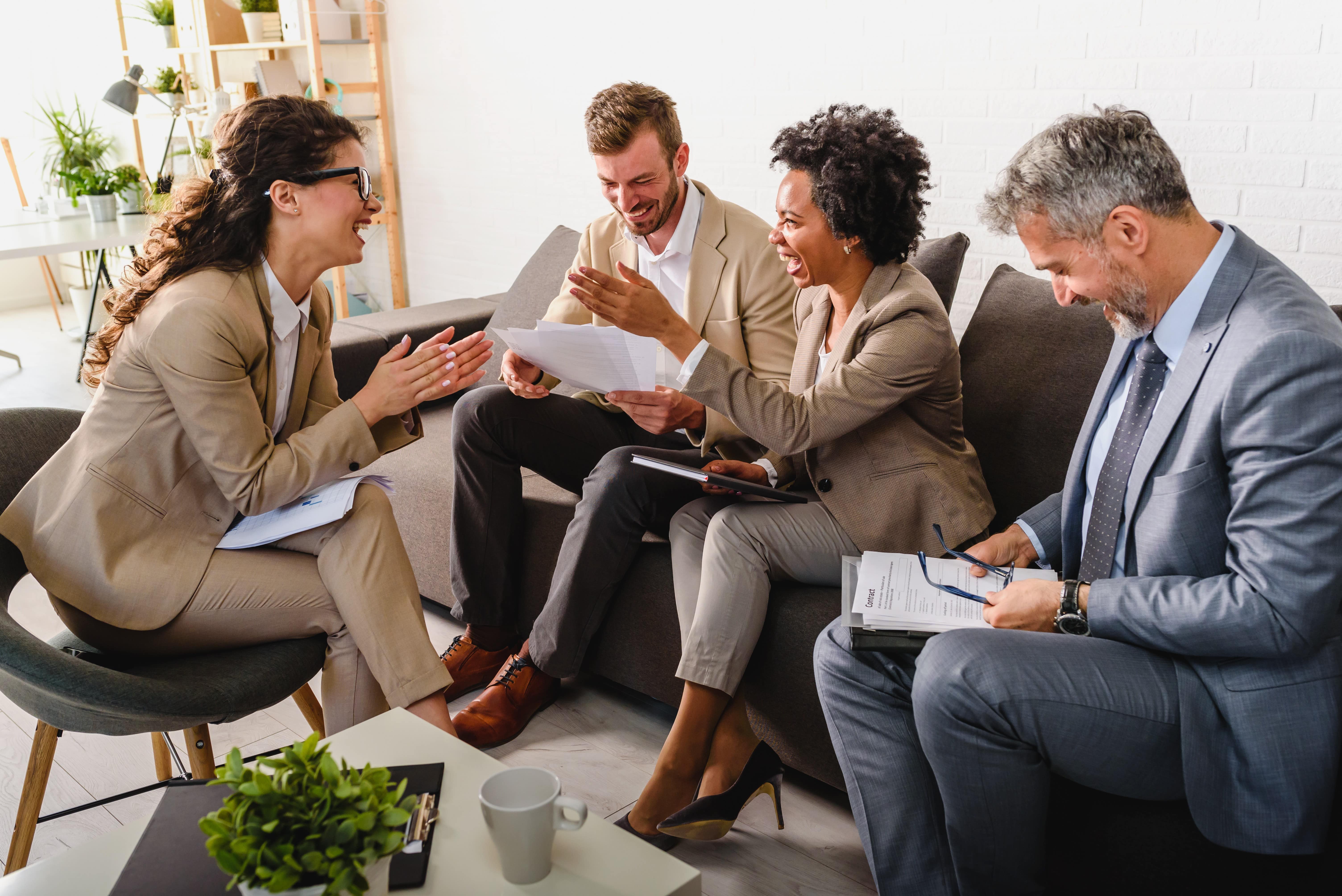 Four diverse business people sitting in a business lounge, engaged in a discussion about leadership and exective coaching and sharing laughter