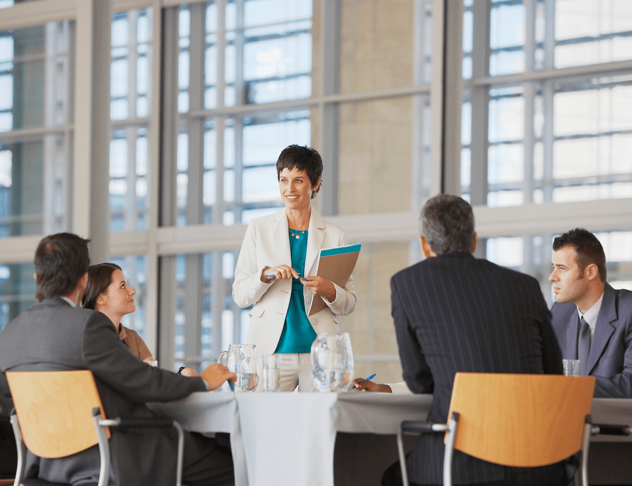 Image showcasing a female coach standing confidently in a boardroom in a coaching session with an executive leadership team, symbolizing empowerment