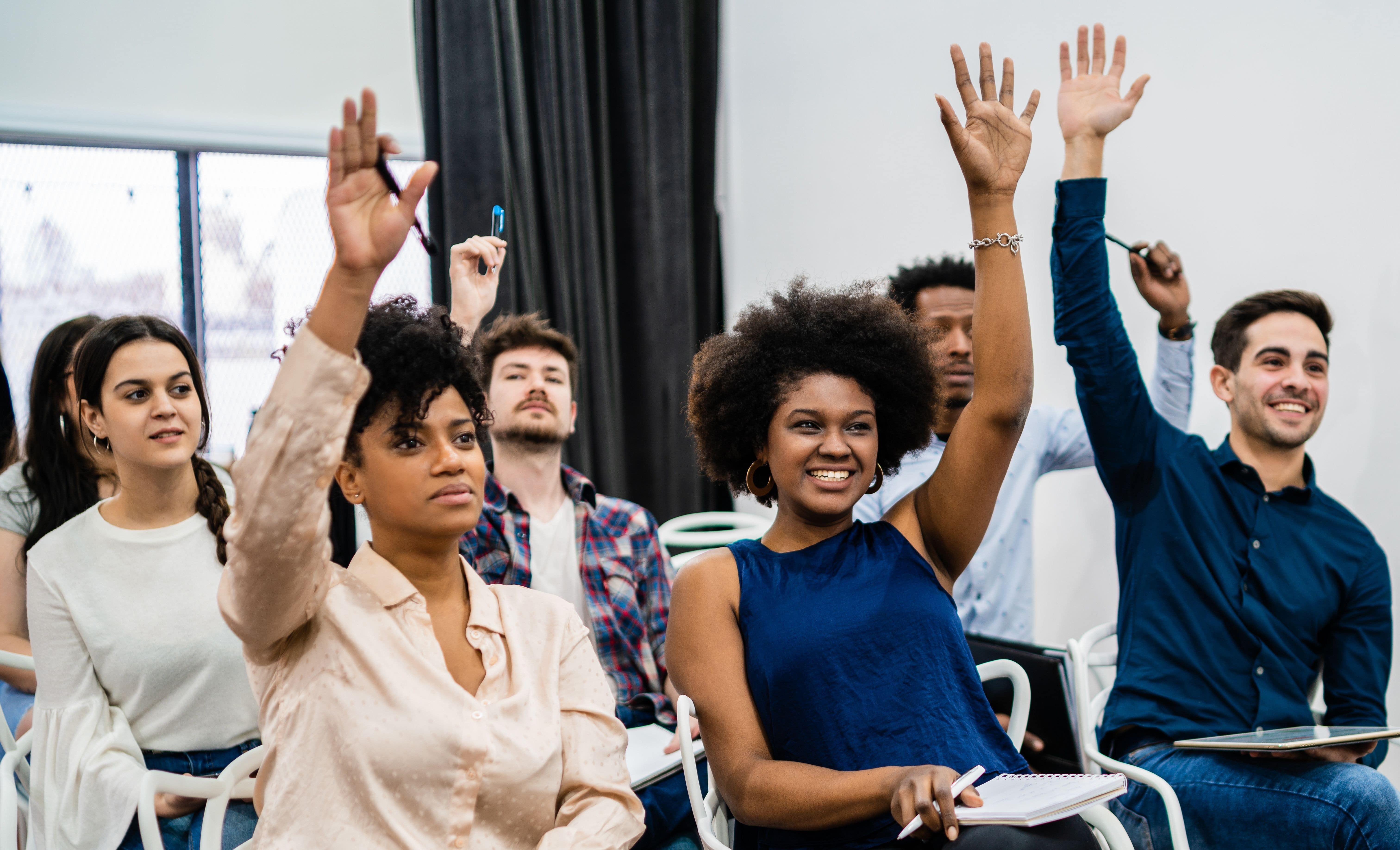 Image of leaders in a room, raising their hands to vote on a decision with smiles on their faces, reflecting a positive and participatory leadership discussion