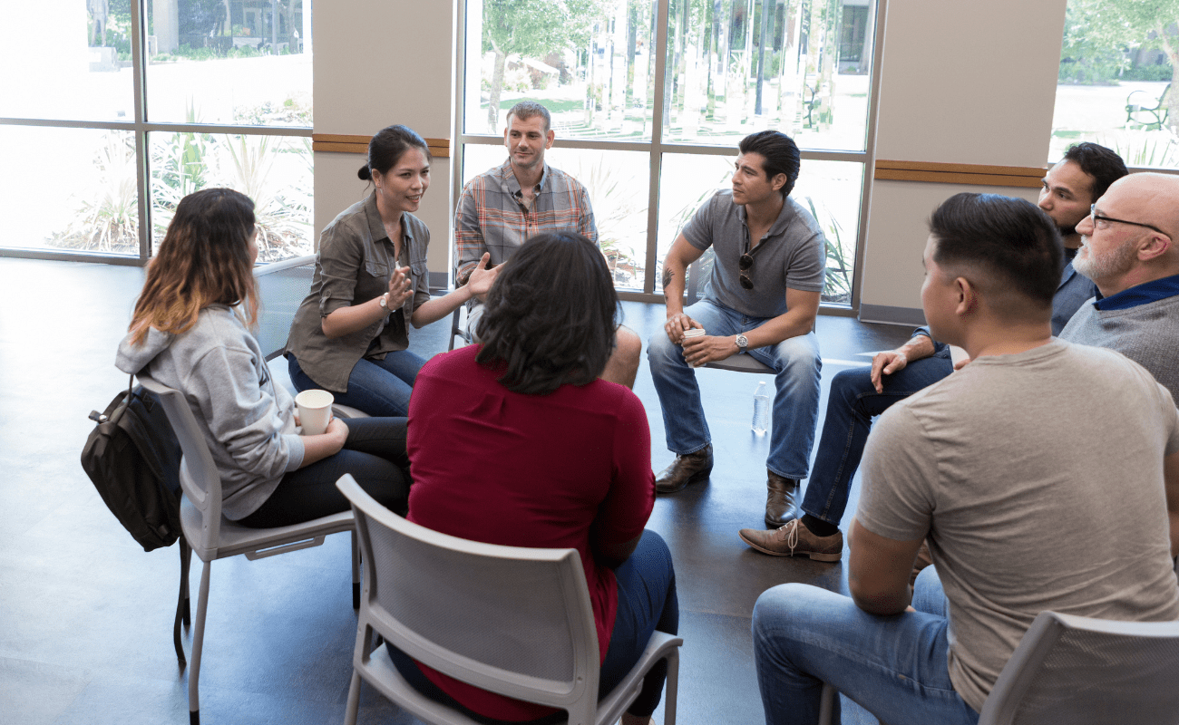 Image of a female coach seated within a circle of a leadership team, delivering an inclusive and interactive coaching session