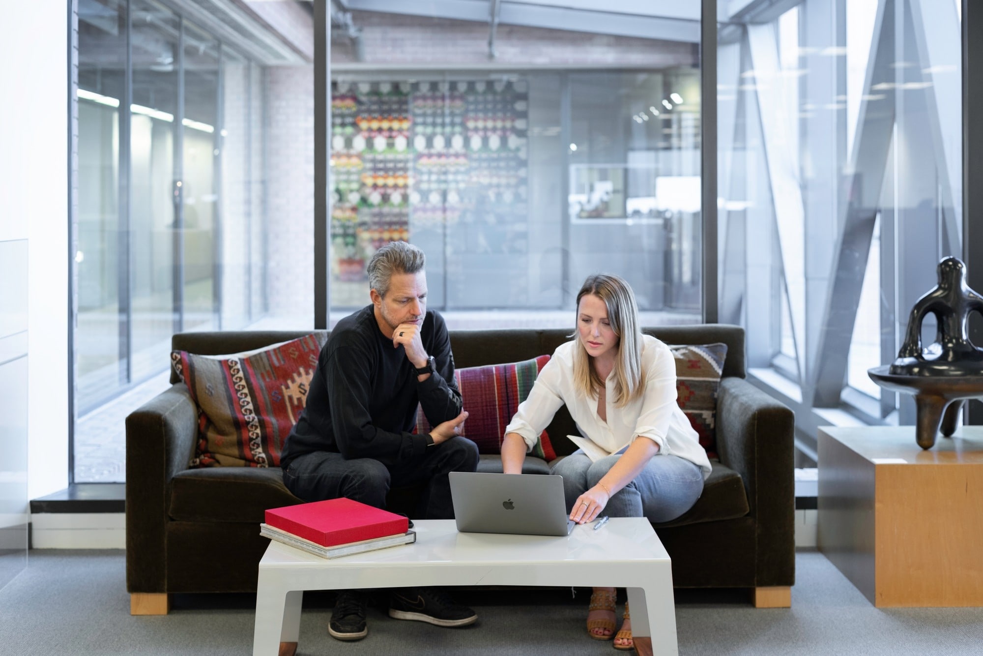 Image of a seasoned executive and a female executive leader seated on a couch, attentively watching a laptop screen, symbolizing a coaching moment