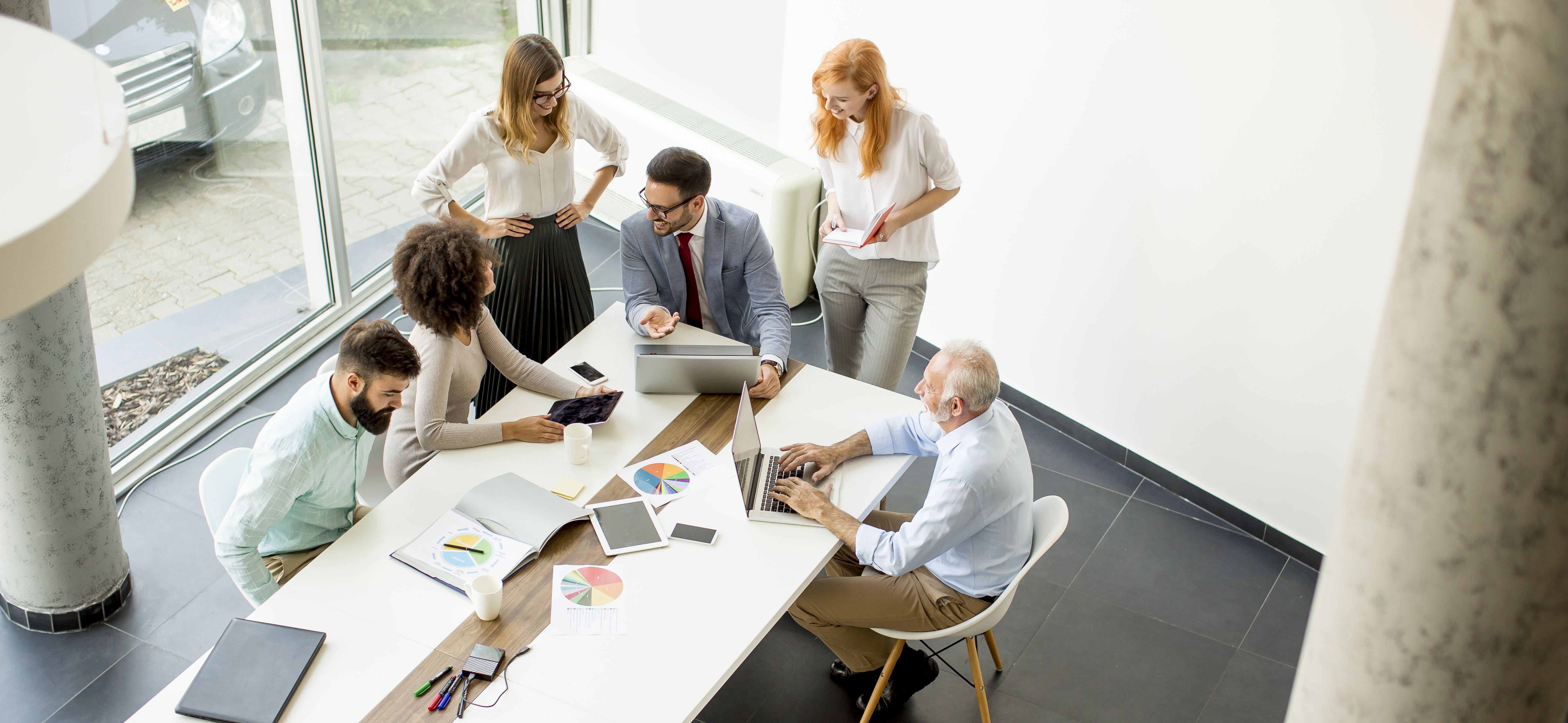 Image of a collaborative scene where a team sits around a table in discussion with their coach, emphasizing teamwork, engagement, and leadership development