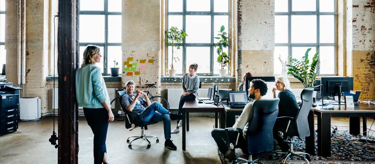 Image illustrating a female coach standing in a meeting room, actively engaging with a leadership team during a collaborative session