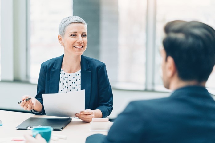 Image of a professional setting where a female executive coach is engaged in a conversation with her male client, focused on empowerment and development